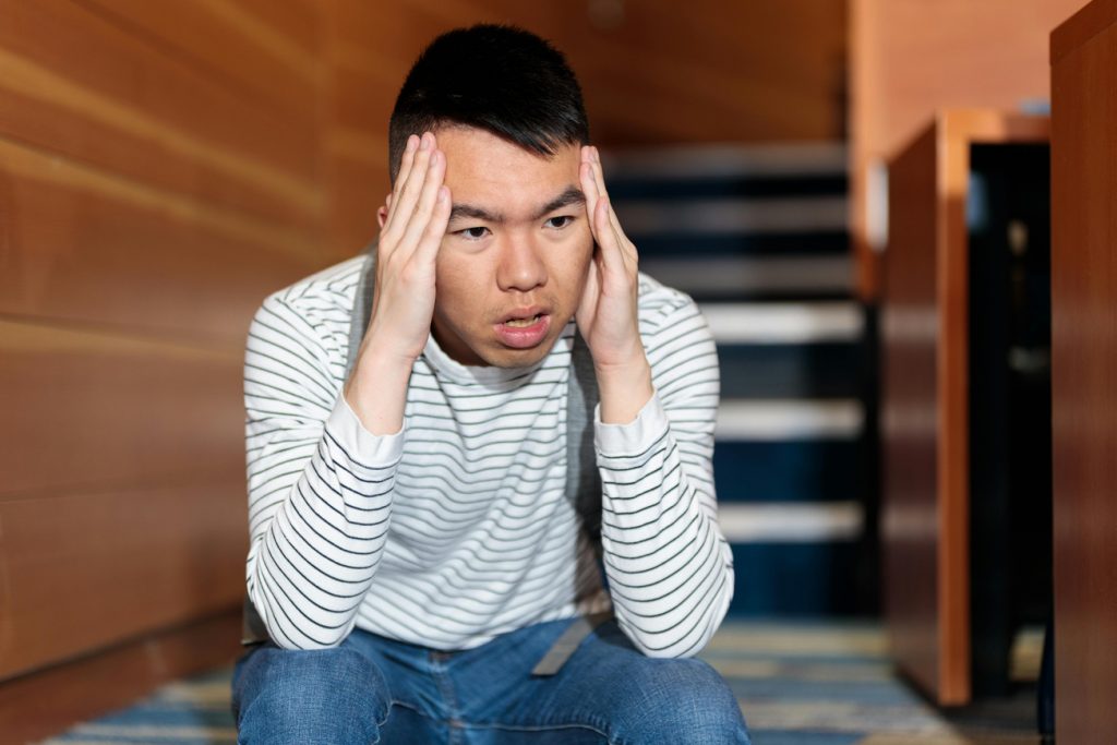 An LGBTQIA+ parent sits alone, head in hands, face showing stress and anxiety. 