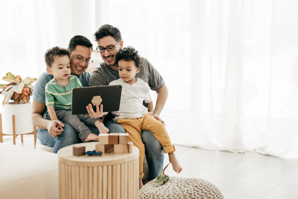 Two LGBTQ+ parents and their children engaging in an online Baby and Parent support group activity conveying affirmation, visibility, and connection.