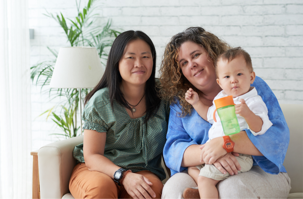 Two mothers sitting together indoors holding their baby and smiling at the camera